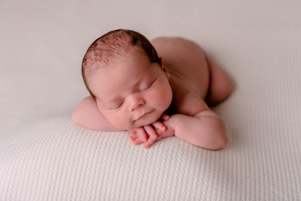 newborn baby sleeping on their hands with a smile