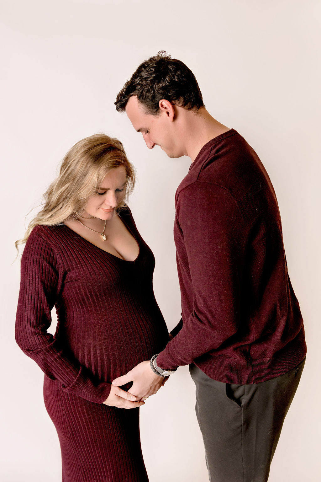 pregnant woman and her partner dressed in matching maroon outfits looking at her baby bump