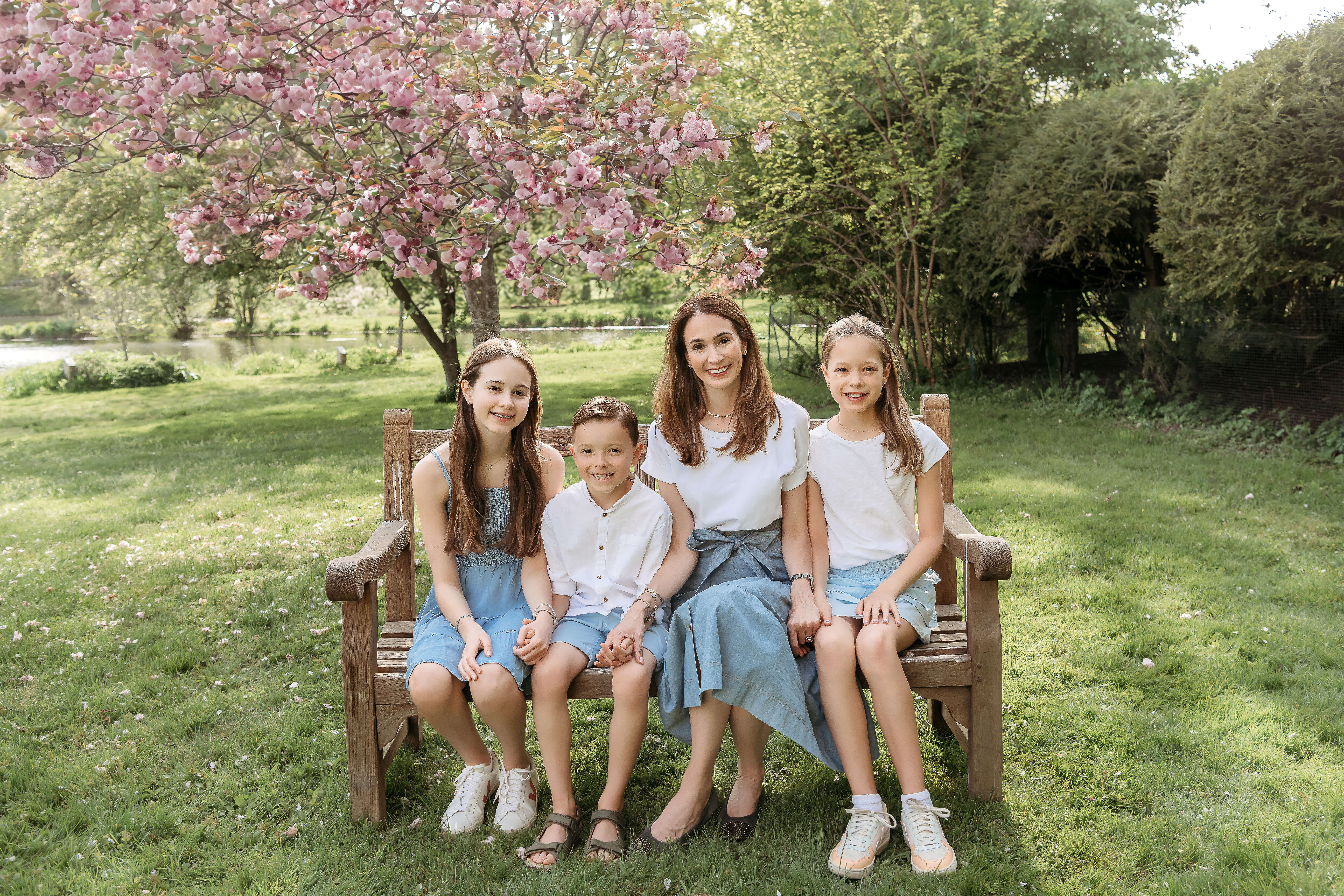 mommy and her children sitting in the bench in front of cherry blossom tree