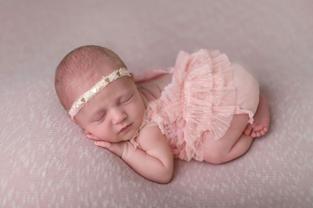 A newborn baby sleeps in froggy pose in a pink dress