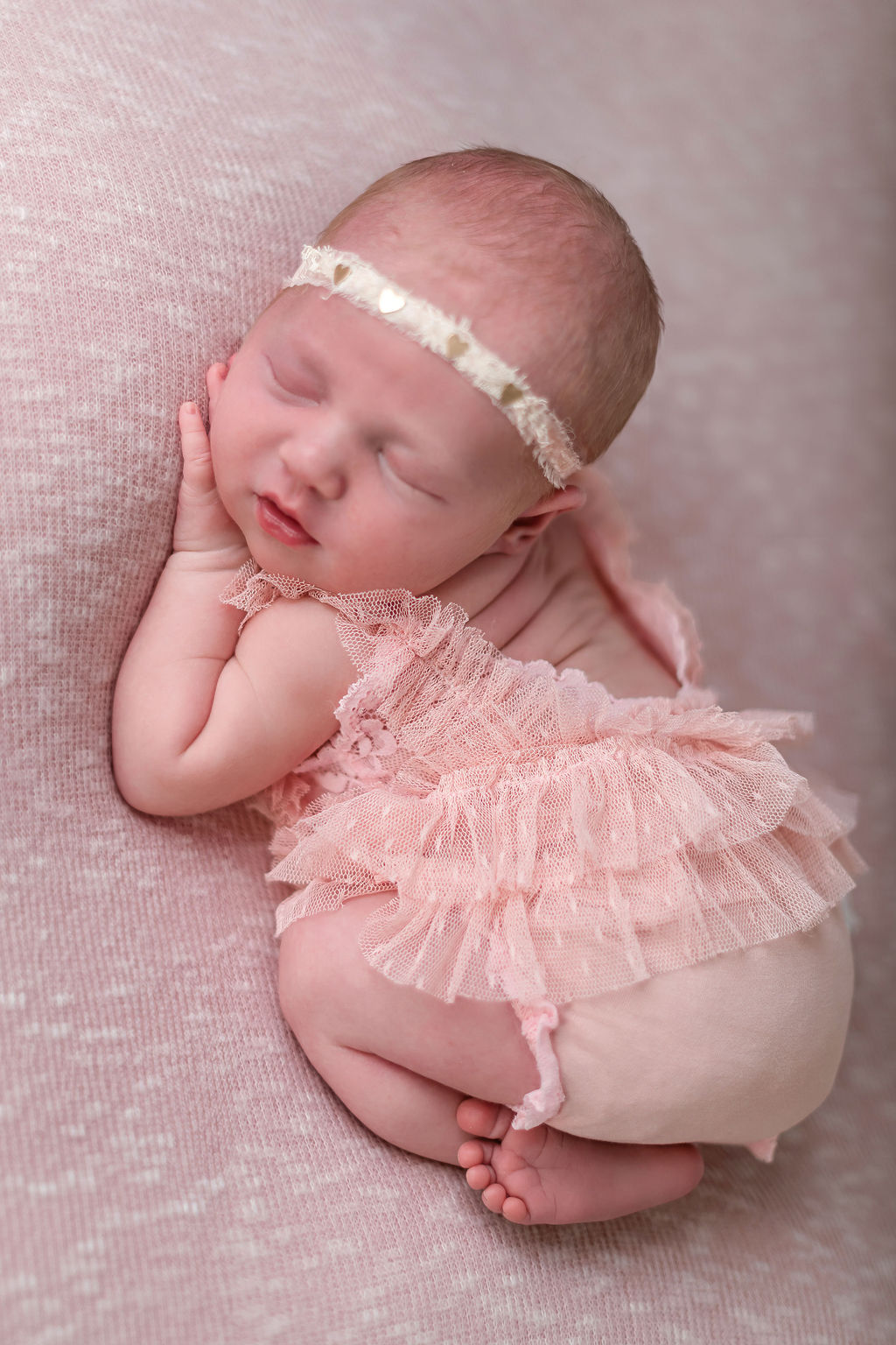 A newborn baby sleeps on a pink bed in a pink dress in froggy pose after mom had prenatal massage stamford ct