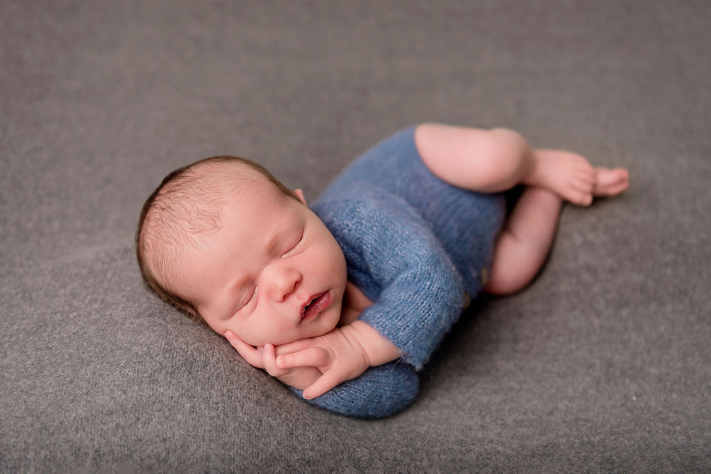 A sleeping newborn baby on his side in a blue knit onesie after visiting pediatricians in Stamford, CT