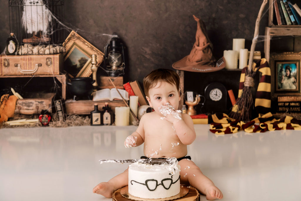 A baby eats a harry potter themed cake while sitting in a studio
