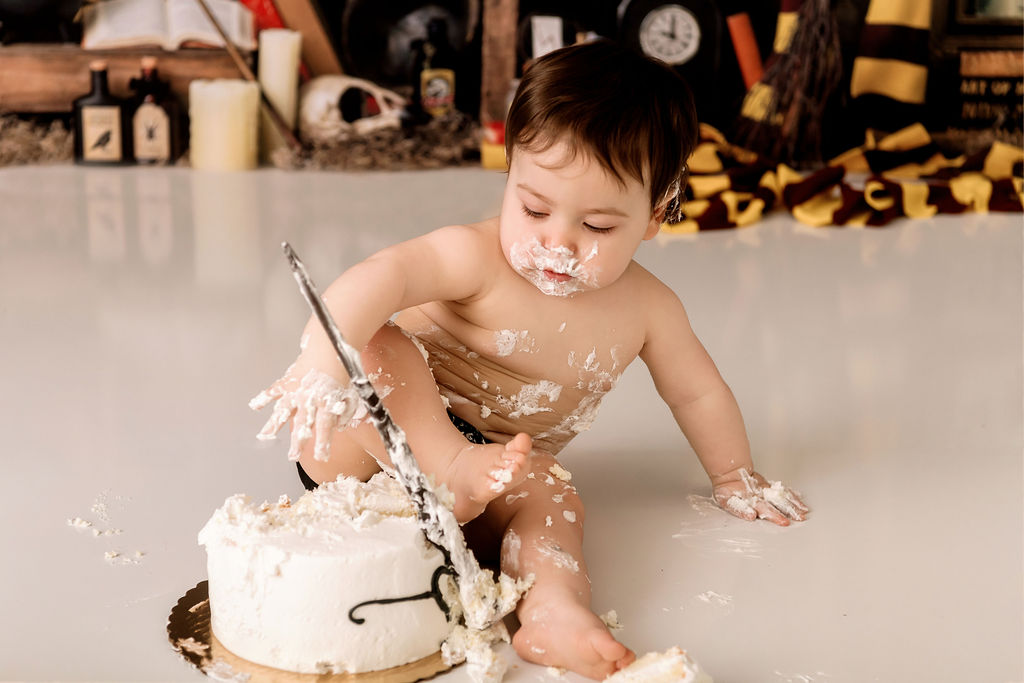A baby smashes a cake in a studio while covered in icing with a wooden magic wand after some baby classes in Stamford, CT