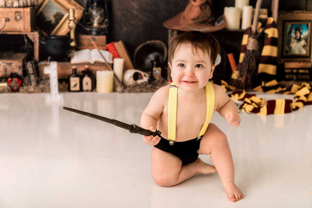 A baby in black shorts and yellow suspenders plays with a wooden wand in a studio after meeting lactation consultants in Stamford, CT