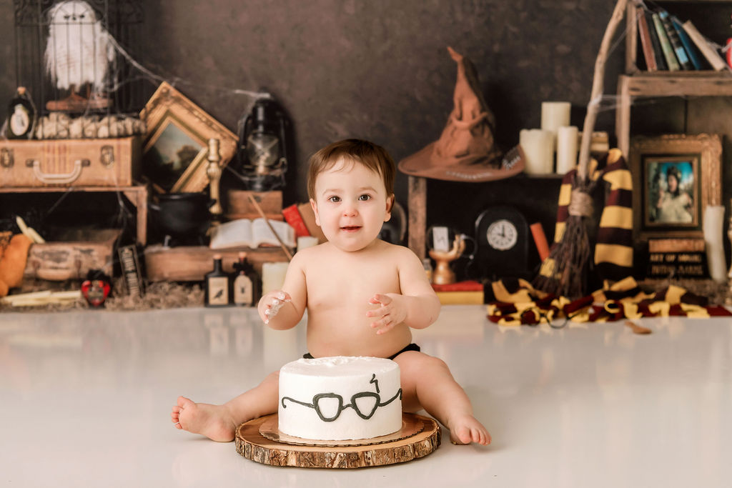 A smiling infant sits behind a harry potter cake on a wood base in a studio with a big smile after meeting lactation consultants in Stamford, CT