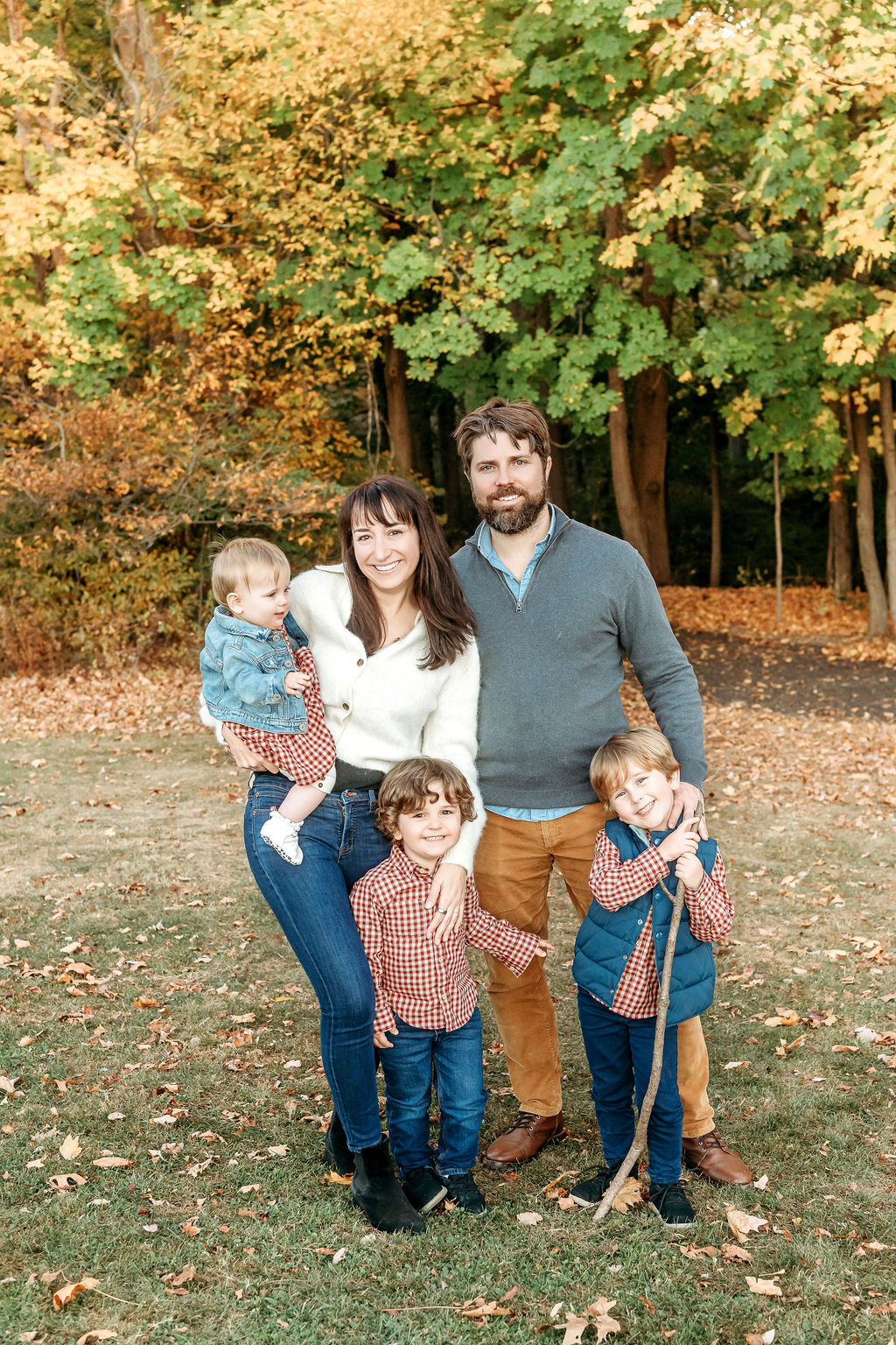 A mom and dad stand in a lawn with their three toddlers in matching plaid and denim in fall after finding nannies in connecticut