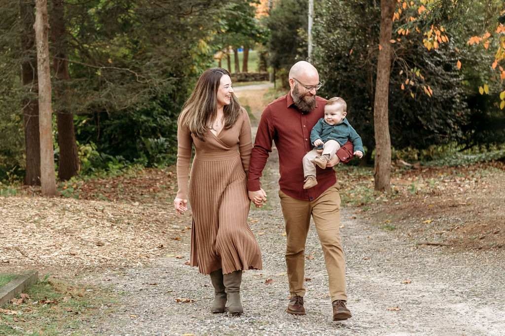 Happy mom and dad hold hands while walking in a park with heir baby in dad's arm in fall thanks to connecticut fertility clinics
