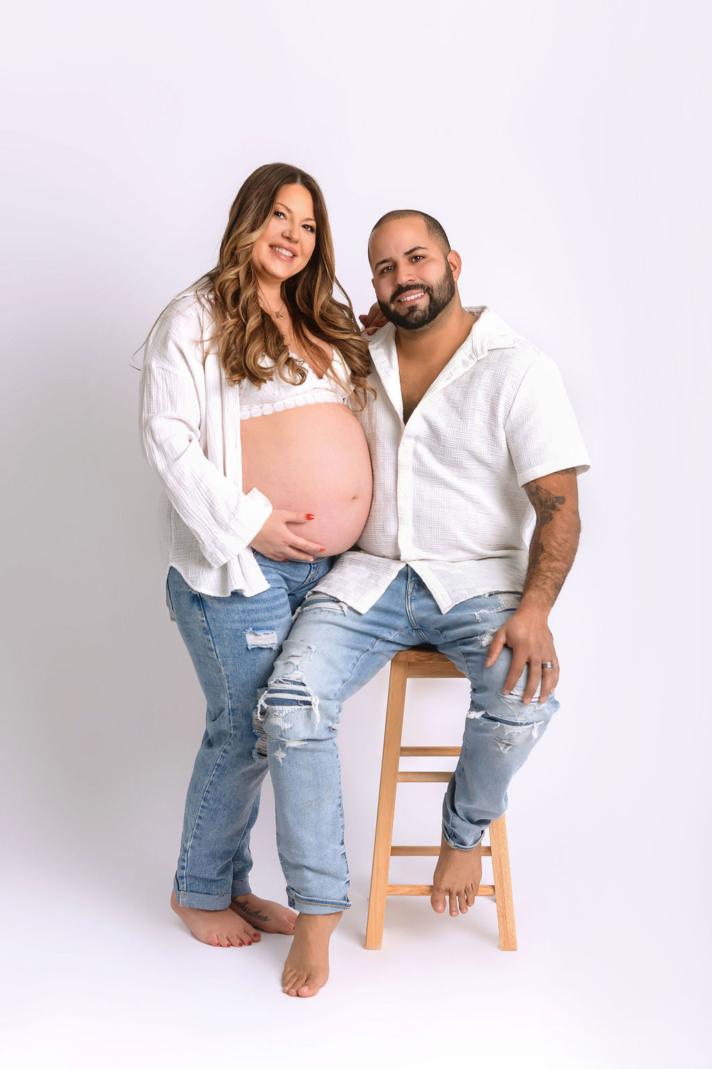 A pregnant couple in white shirts and jeans in a studio