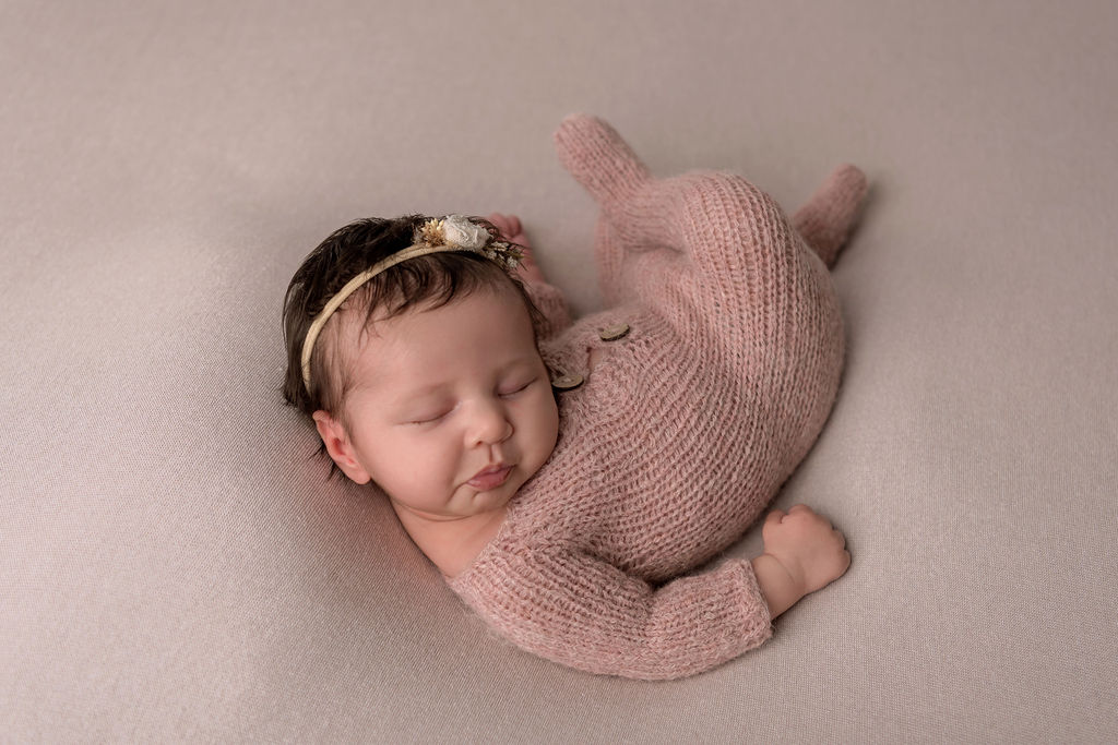 A newborn baby sleeps curled up in a pink knit onesie after meeting doulas in Stamford, CT