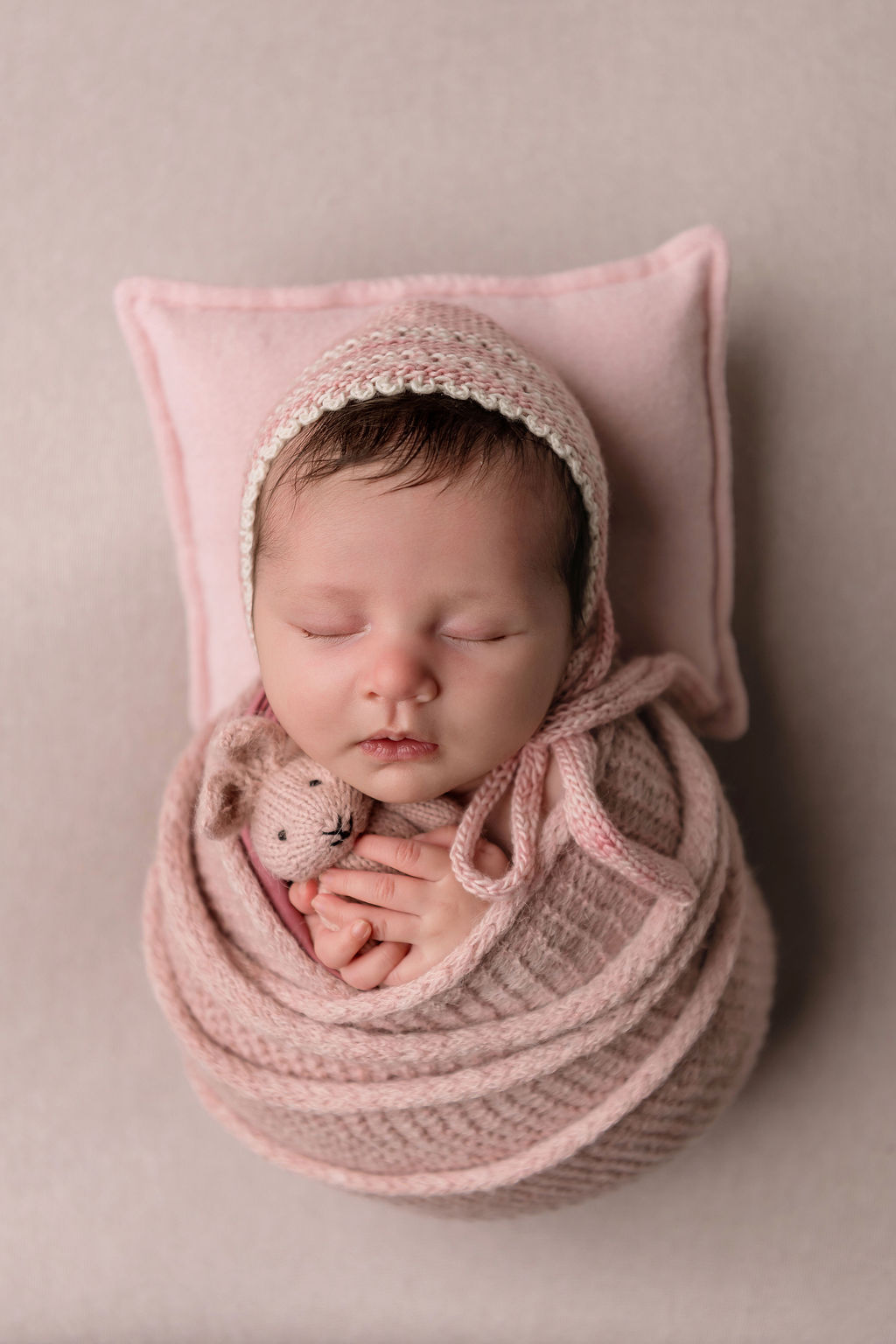 A newborn baby sleeps in a pink knit swaddle holding a teddy after enjoying doulas in Stamford, CT