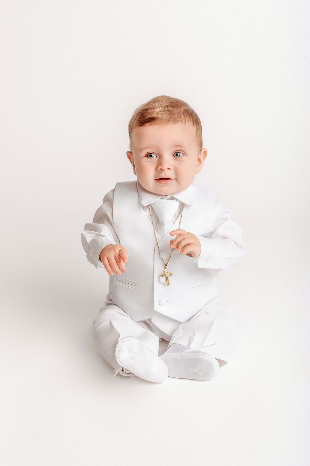 A toddler in a white suit and vest with gold chain sitting in a studio before visiting children's museums in connecticut