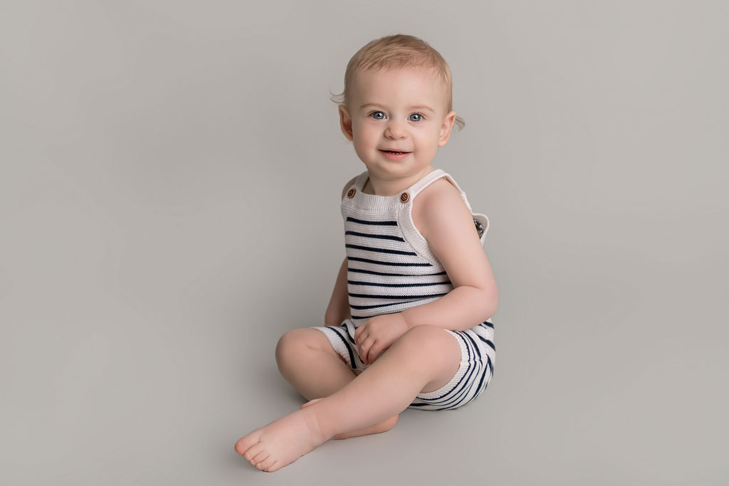A toddler in stripe onesie overalls sits smiling in a studio after visiting a toy store in stamford ct